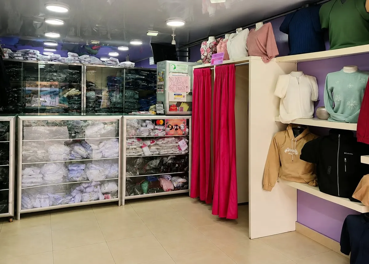 Otra vista del interior, con vitrinas de camisas blancas, dos vestidores con cortina roja y estantería de chaquetas y sacos