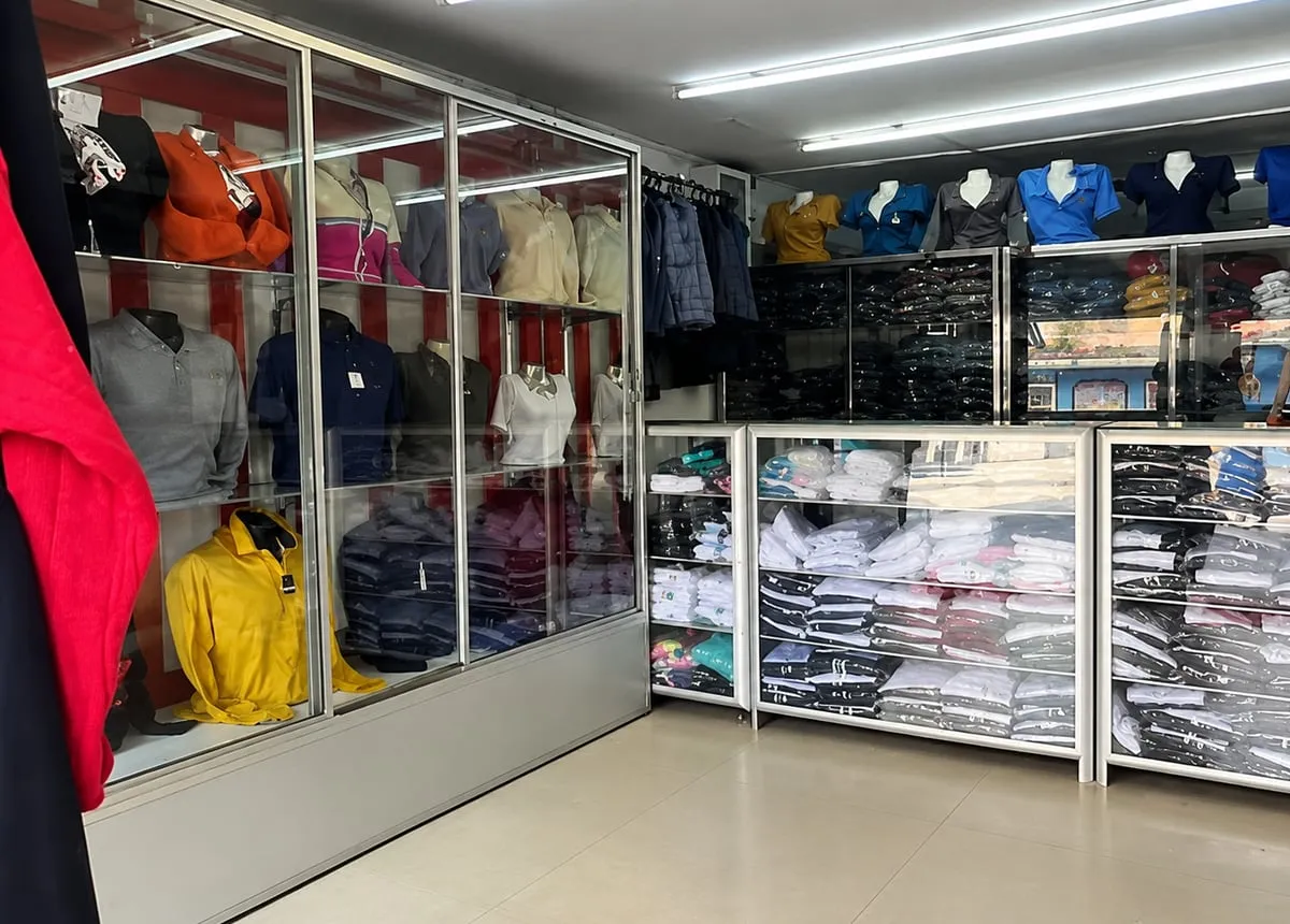 Interior de la tienda con vitrinas de vidrio llenas de camisas y polos doblados, y maniquíes con uniformes de trabajo sobre los estantes